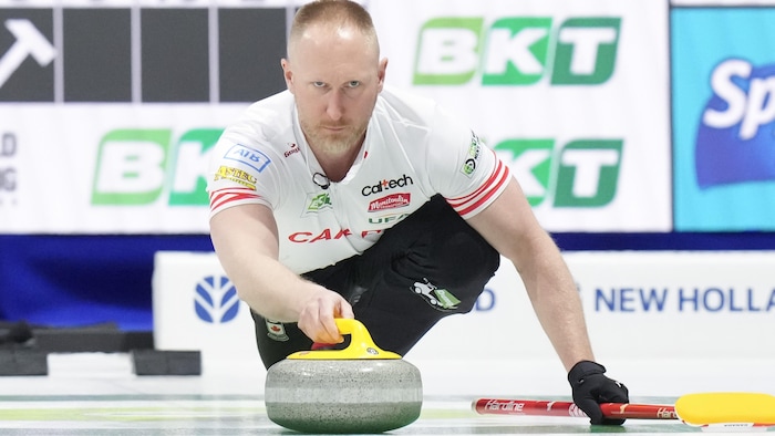 Un joueur de curling fait glisser sa pierre sur la glace.