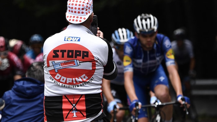 Un passionné de cyclisme, vêtu d'une veste sur laquelle on peut lire « Arrêtez de vous doper», photographie les coureurs à leur passage.