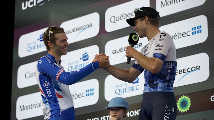 Sur un podium, il serre la main d'un autre cycliste.