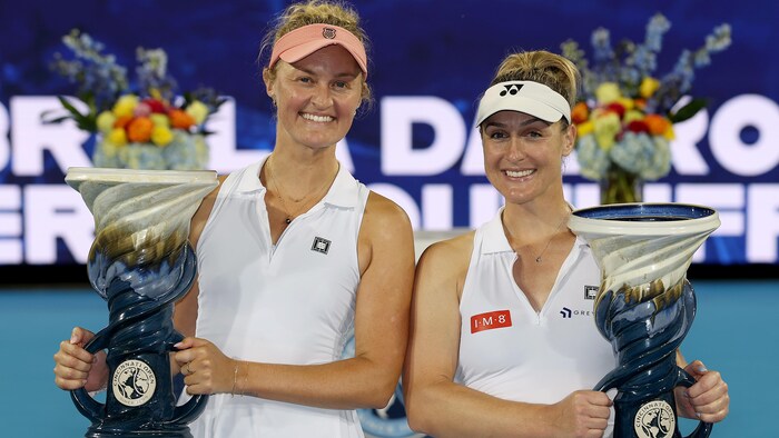 Deux joueuses de tennis sourient en tenant leur trophée. 