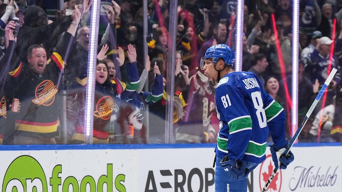 Un hockeyeur célèbre un but pendant que des supporteurs sautent de joie.