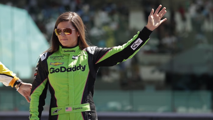 Une femme pilote en combinaison de course salue la foule.
