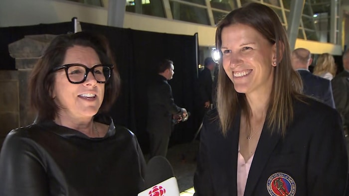 Deux femmes souriantes parlent dans micro de Radio-Canada lors d'une soirée mondaine.