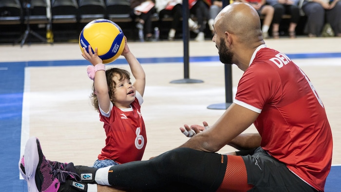 Danny Demyanenko assis au sol avec sa fille qui tient un ballon.