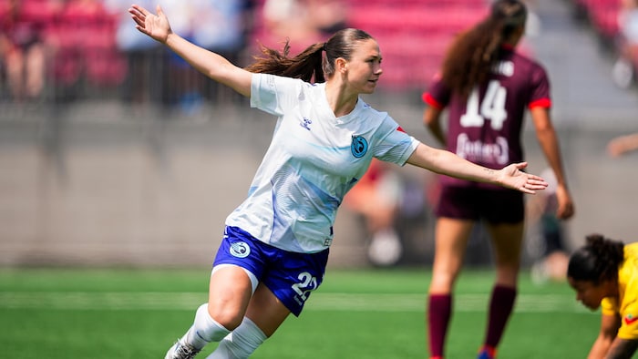 Une jeune femme tribunal les bras dans les airs après avoir marqué un but au soccer.