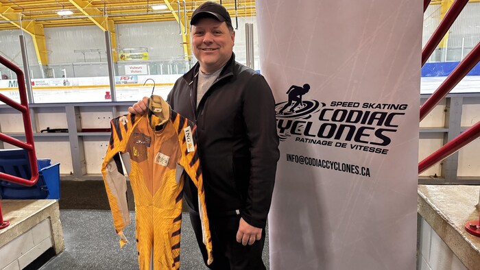Homme debout avec un costume de patinage de vitesse jaune et orange.