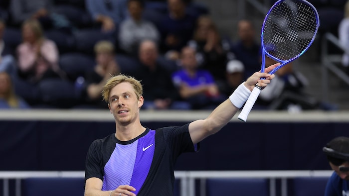 Un joueur de tennis lève sa raquette en l'air pour saluer la foule, après une victoire.