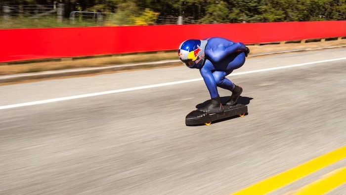 Un homme en position aérodynamique sur sa planche à roulettes, à pleine vitesse.