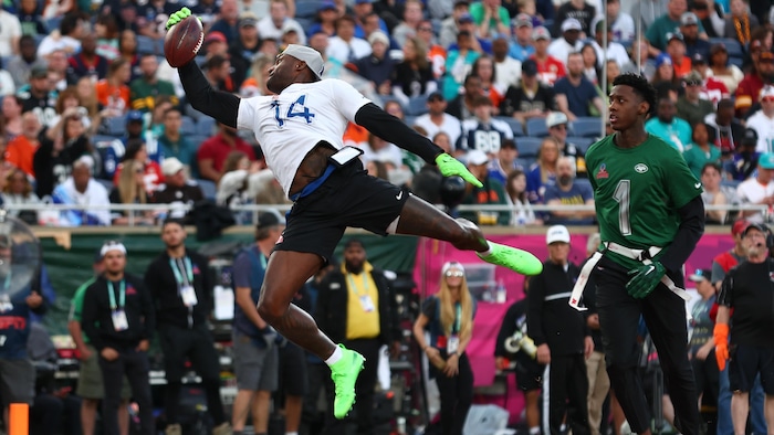 Un joueur de flag football effectue un attrapé spectaculaire d'une seule main, la droite, en plongeant, devant un rival le regardant.