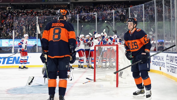 Two disappointed hockey players while their opponents celebrate their victory further. noah dobson, little story smoking