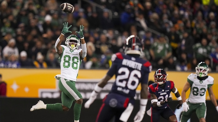 A footballer tries to catch a ball in front of two rivals.