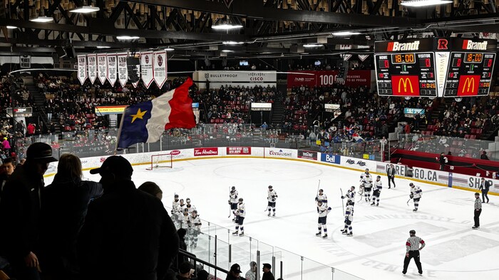 Un drapeau acadien est agité dans les estrades pendant que les joueurs sortent de la patinoire.