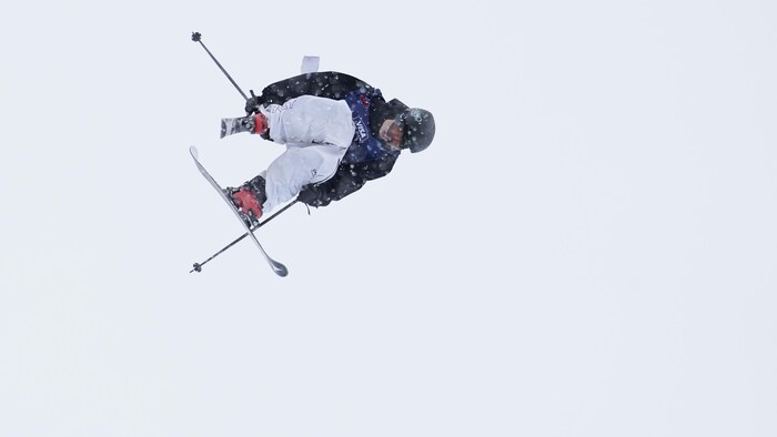 Le skieur de 18 ans est en plein vol plané et effectue une figure en tenant son ski droit avec sa main droite.