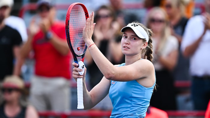 Une joueuse de tennis applaudit en frappant sa raquette de la main gauche.