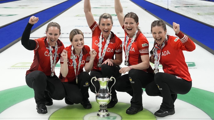 Des joueuses de curling autour d'un trophée avec leurs bras dans les airs. 