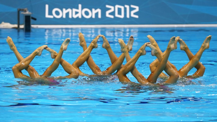Des nageuses artistiques font une figure la tête dans l'eau.