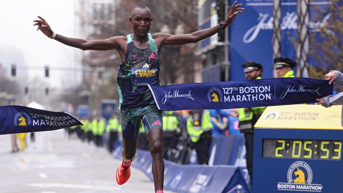 Un homme lève les bras et déchire le ruban à l'arrivée d'un marathon.