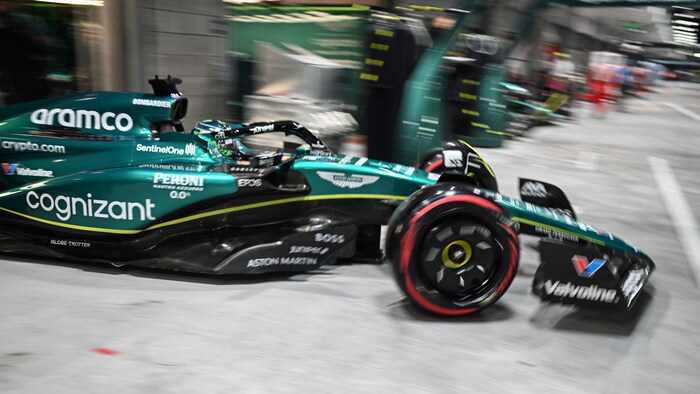 Une monoplace de F1 sort d'un garage illuminé.