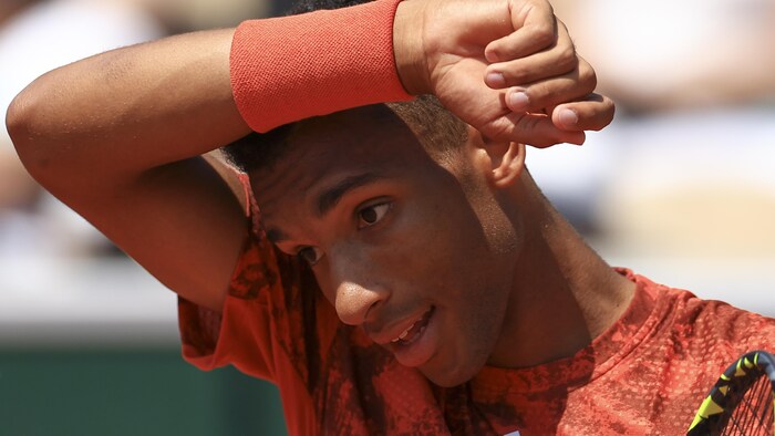 Le joueur de tennis s'essuie le front avec son bras droit.