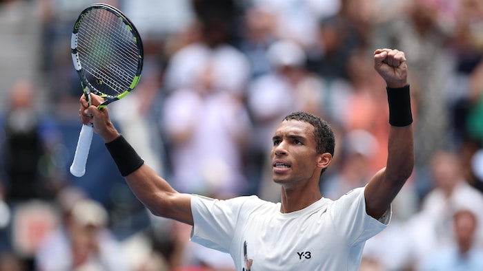 Un joueur de tennis lève les bras avec sa raquette dans la main   droite.