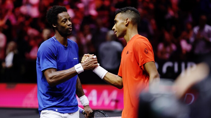 Deux joueurs de tennis, l'un vêtu de bleu et l'autre de rouge, se serrent la main après un match au filet. 