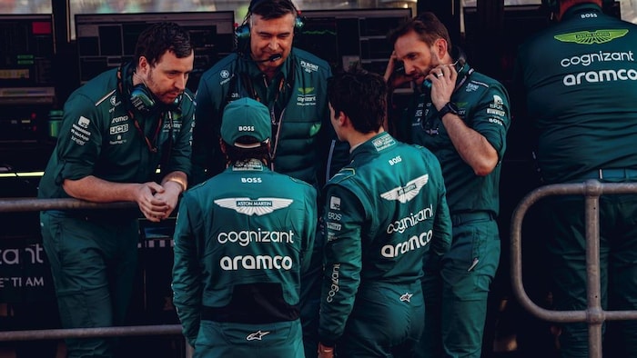 Deux pilotes de F1, de dos, discutent avec des membres de leur équipe.  