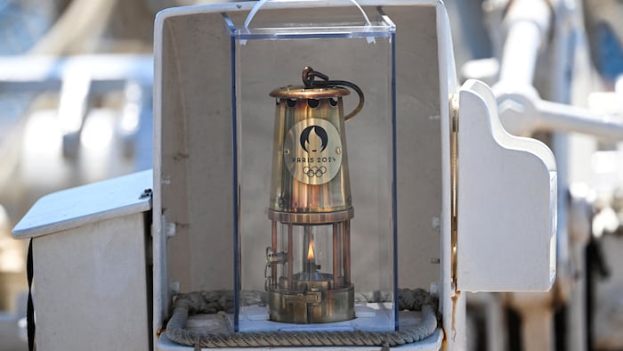Une flamme brûle dans une lanterne de métal portant le sigle des Jeux olympiques de Paris.