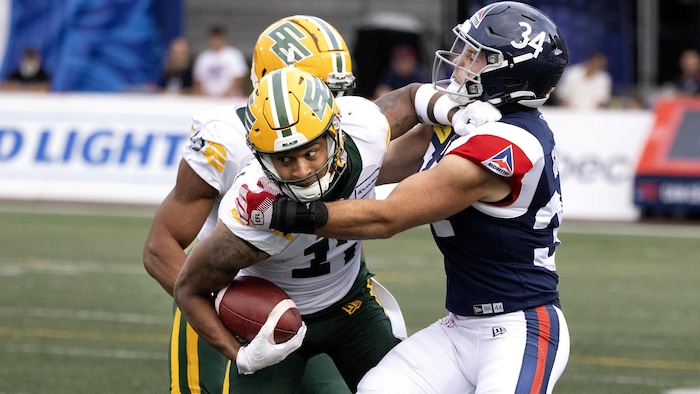 Un joueur de football des Elks d'Edmonton tente d'éviter un plaqué d'un joueur des Alouettes de Montréal.