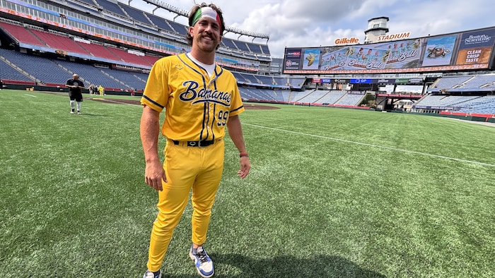 Un joueur de baseball se tient debout sur le terrain, regarde la caméra et sourit.