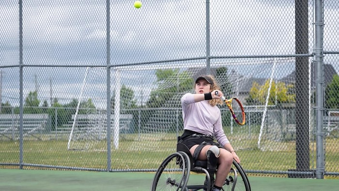 Une joueuse de tennis en fauteuil roulant se prépare à retourner une balle dans les airs. 