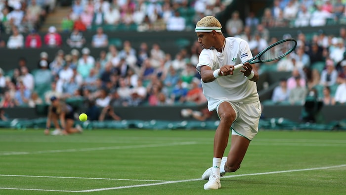 Un joueur de tennis retourne une balle sur le gazon.