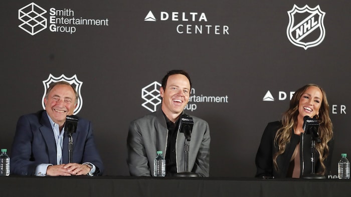 Trois personnes devant un micro rient lors d'un point de presse.
