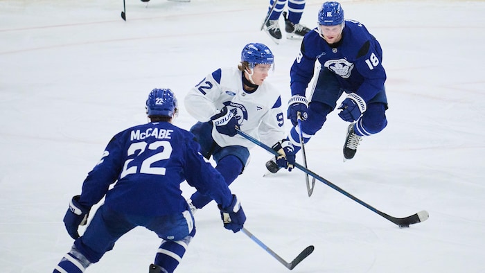 Un joueur de hockey tente de se faufiler entre deux adversaires avec la rondelle.