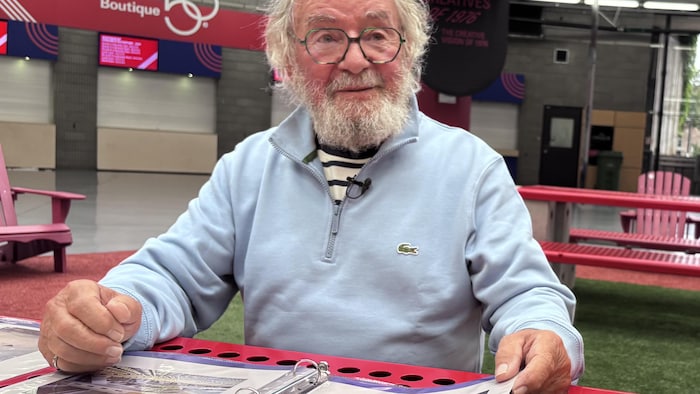 Assis à une table, il feuillette un cahier.