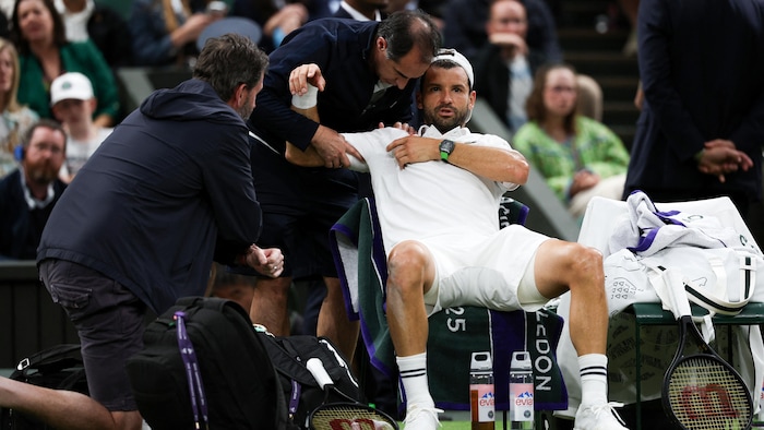 Le joueur est assis en bordure du terrain pendant qu'un thérapeute s'affaire sur lad épaule droite.