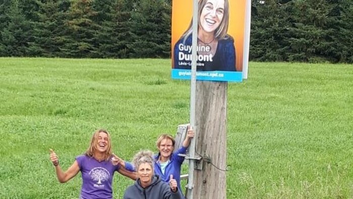 Guylaine Dumont posa con dos mujeres en un campo frente a su cartel electoral.