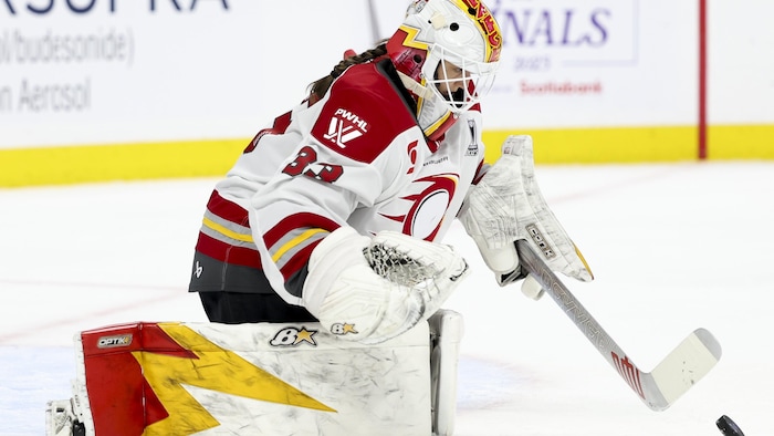 Une gardienne de but au hockey sur ses genoux, regarde la rondelle. 