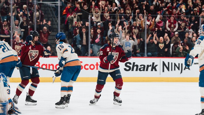 Une joueuse de hockey célèbre un but devant la foule et d'autres joueuses. 