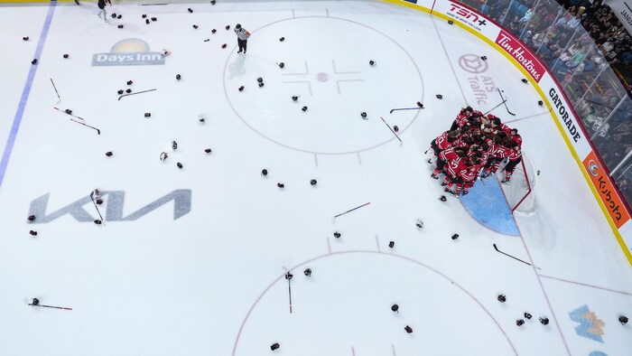 Des joueurs réunis autour de leur gardien de but se réjouissent, entourés de gants et de bâtons éparpillés tout autour sur la patinoire.