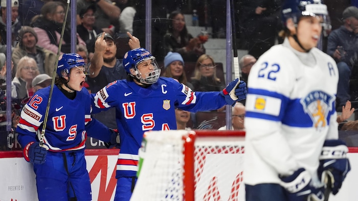 Two hockey players celebrate a goal in front of an opponent.