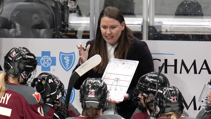 Une entraîneuse de hockey donne des consignes à ses joueuses sur un tableau.