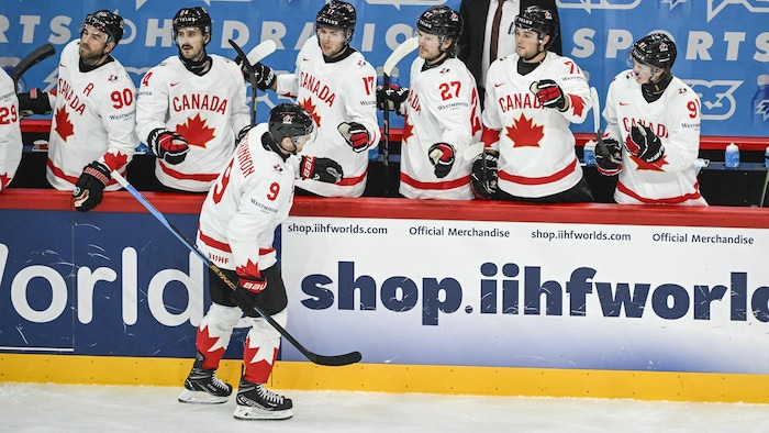 Un joueur de hockey du Canada donne la main à ses coéquipiers au banc des joueurs.