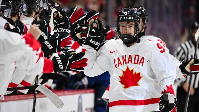 Un hockeyeur du Canada donne la main à ses coéquipiers au banc des joueurs.