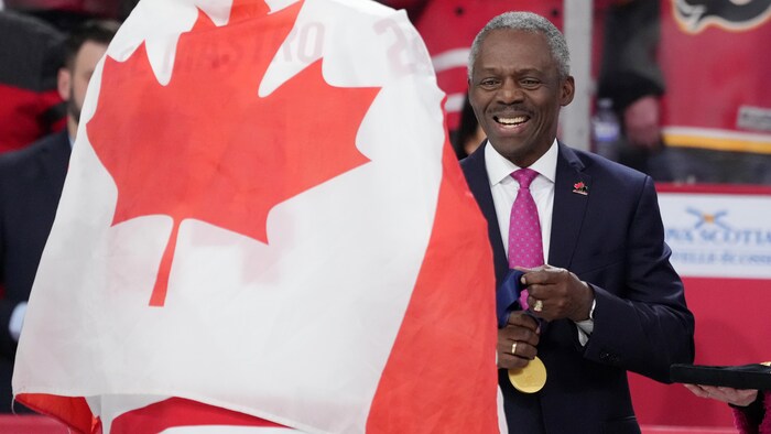 Souriant, il tient une médaille d'or à côté d'un joueur enveloppé dans un drapeau canadien.