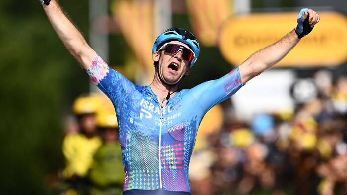 Le cycliste lève les bras vers le ciel après sa victoire.