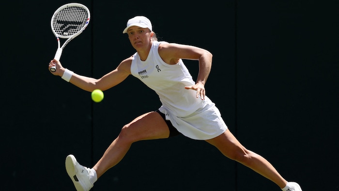 Une joueuse de tennis en blanc s'étire pour atteindre une balle. 