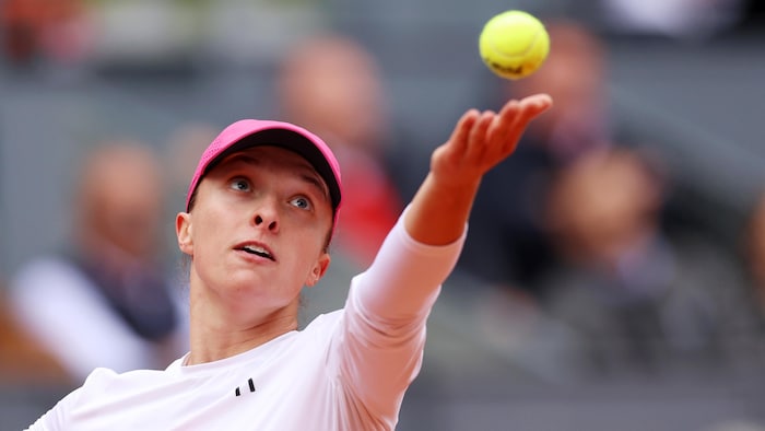 Une joueuse de tennis au service lance une balle de la main gauche et regarde en l'air.