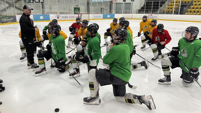 Un entraîneur parle à ses joueurs, agenouillés devant lui, pendant une séance de patinage.