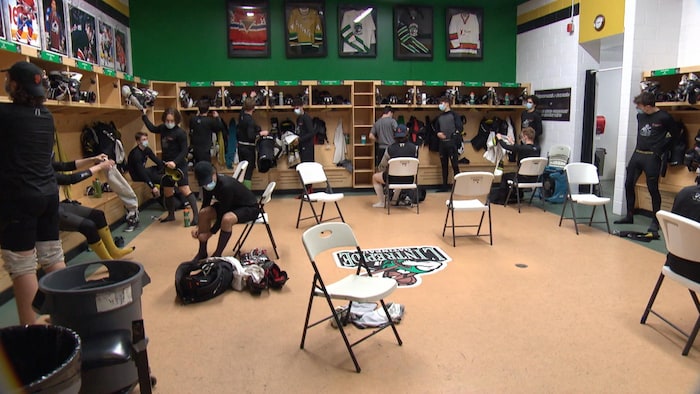Des joueurs se changent dans un vestiaire de hockey. Ils respectent tous une distance de deux mètres entre eux.