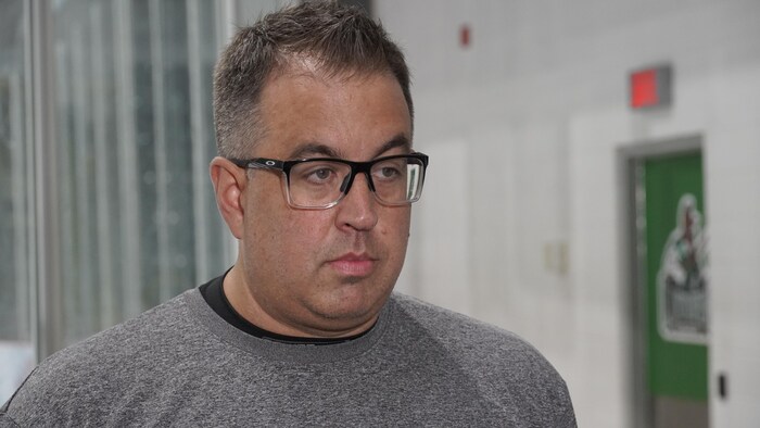 Un entraîneur de hockey répond aux questions d'un journaliste devant la porte d'entrée de son vestiaire.